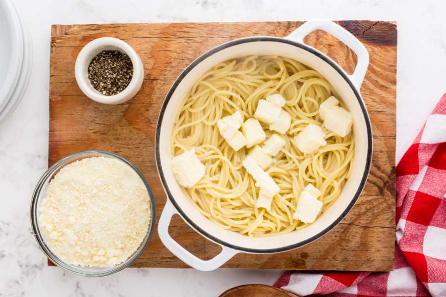 adding tabs of butter to pot with pasta