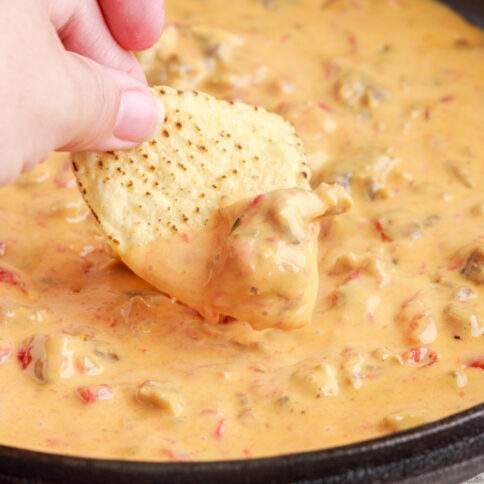 Cheesy Sausage Rotel Dip in a pan with a chip