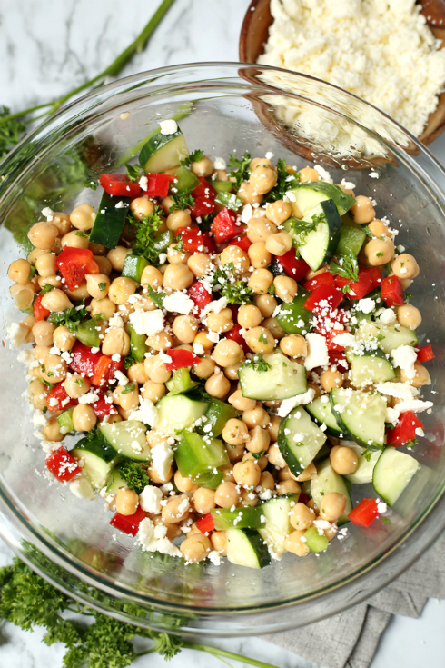 Cucumber Chickpea Salad - cheese sprinkled on mixed salad in glass bowl - Family Fresh Meals