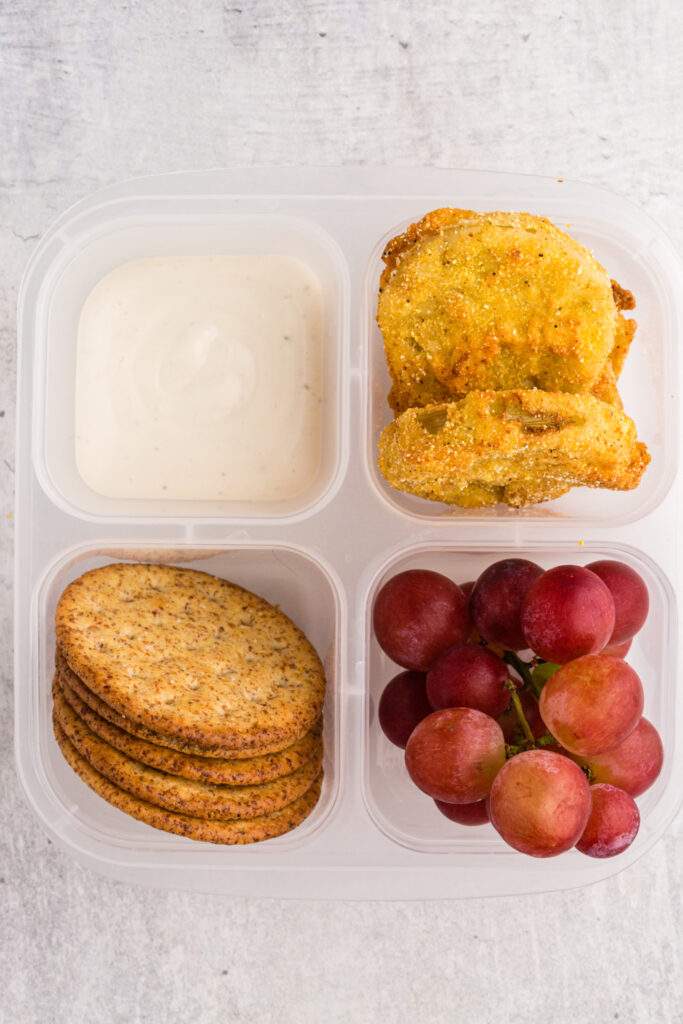 fried green tomatoes packed in a lunch box with dip, crackers and grapes