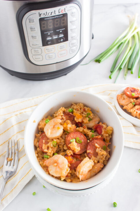 Jambalaya in a white bowl with pressure cooker in background