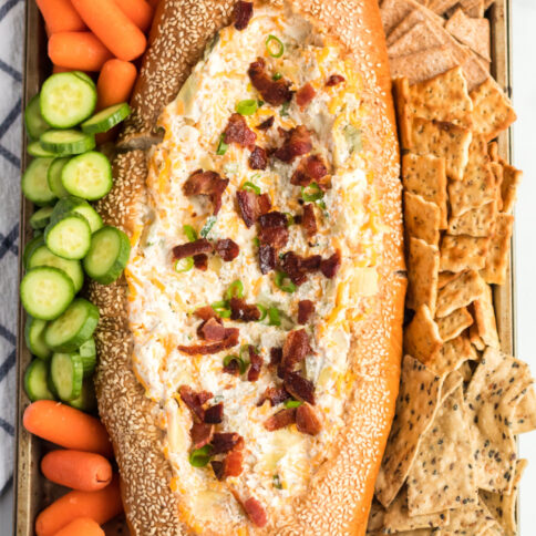 Mississippi Sin Dip in a bread loaf, surrounded by veggies and crackers