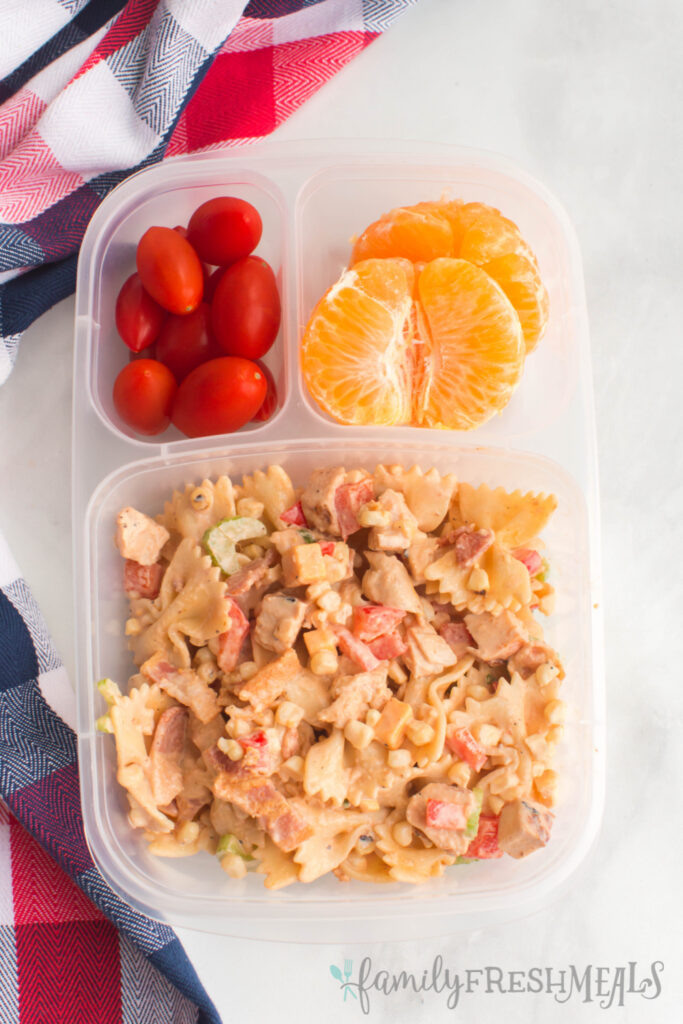 bbq chicken pasta salad packed in a lunchbox with orange slices and cherry tomatoes