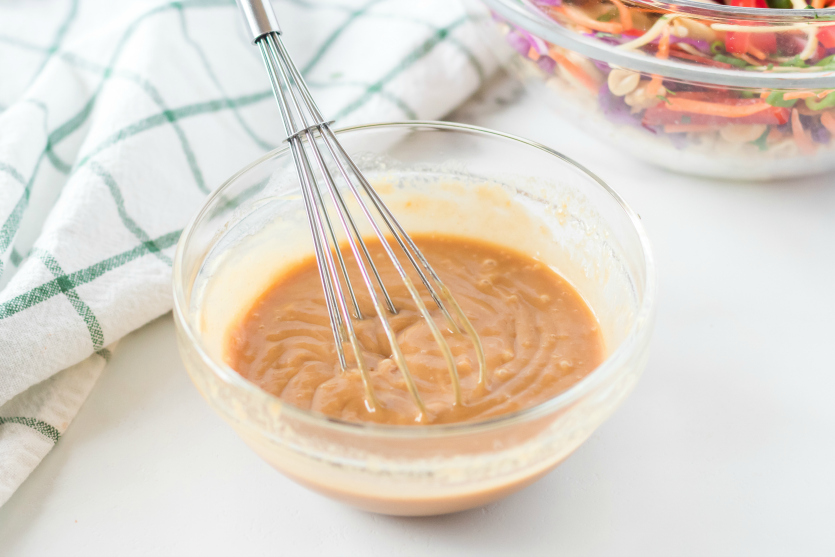 Thai Spaghetti Pasta Salad creamy peanut dressing mixed in a small bowl with a whisk